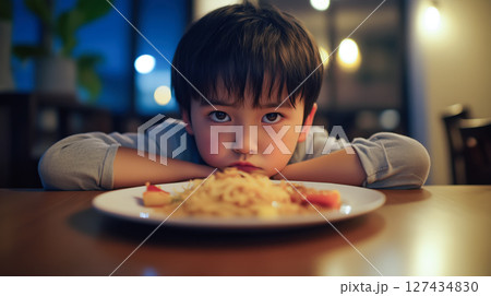 Little boy with no appetite sadly staring at his untouched food on a plate, resting his head on arms at dinner table. Poor appetite concept. Evening atmosphere. Little boy with no appetite sadly staring at his untouched food on a plate, resting his head on arms at dinner table. Poor appetite concept. Evening atmosphere. 127434830