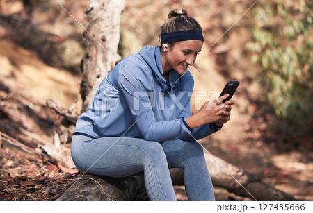 Fitness, woman with smartphone and earphones for music search, run in the woods with technology and audio streaming for workout. Wellness, happy and runner with radio app and exercise outdoor. 127435666