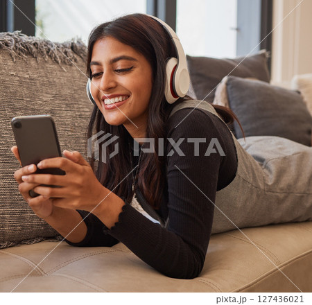 Woman, phone and headphones for listening to music online for happiness, calm and peace while streaming on audio app on home and living room sofa. Female watching video or movie on internet with 5g 127436021