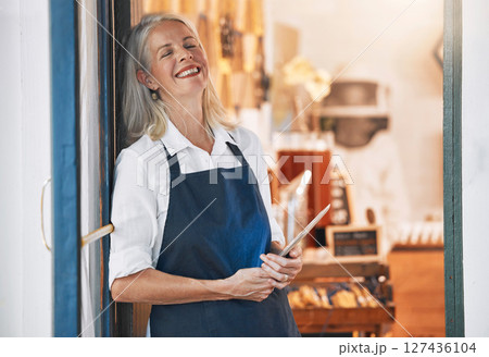Happy senior business owner with a tablet in her store for startup with technology or mobile device. Leader, entrepreneur and elderly woman standing by an open door to welcome customers in the shop. Happy senior business owner with a tablet in her store for startup with technology or mobile device. Leader, entrepreneur and elderly woman standing by an open door to welcome customers in the shop. 127436104