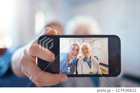 Phone, nurse and happy old woman take a selfie on screen after consulting with medical doctor. Photo, caregiver and healthy senior person in retirement take pictures for social media in nursing home 127436622