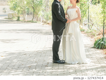 公園の並木道を手を繋いで歩くドレス姿のカップル（ウェディング・ウェディングフォト・新郎新婦） 127437414