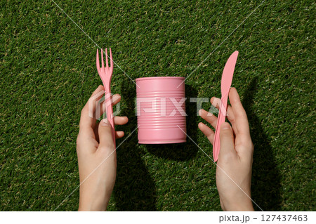 Pink tin can and plastic cutleries in hands on green background, top view Pink tin can and plastic cutleries in hands on green background, top view 127437463