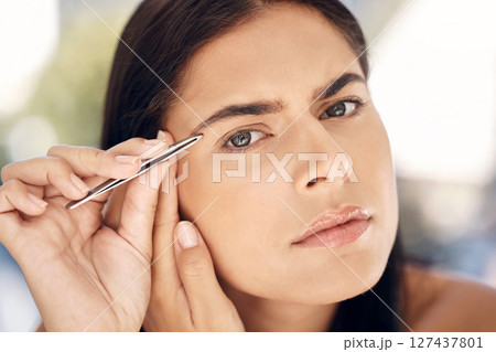 Woman in mirror plucking eyebrows with tweezers and grooming facial routine in morning. Beauty, skincare and tweezing eyebrow hair, portrait of Indian woman face in reflection in bathroom treatment. 127437801