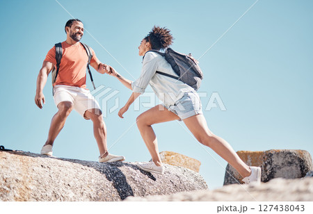 Helping hand, couple and rock climbing or hiking in nature on vacation, holiday or trip. Teamwork, support and traveling man and woman outdoors in countryside mountain climbing, exercise or workout. 127438043