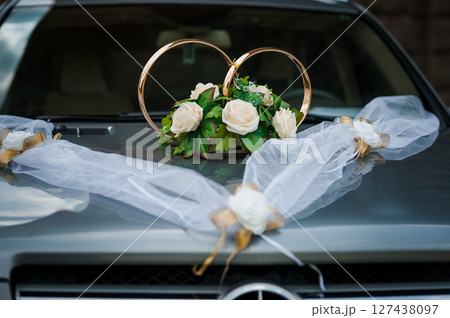 Wedding car decoration with gold rings and white flowers on the hood, draped with sheer white fabric, symbolizing love. Wedding car decoration with gold rings and white flowers on the hood, draped with sheer white fabric, symbolizing love. 127438097
