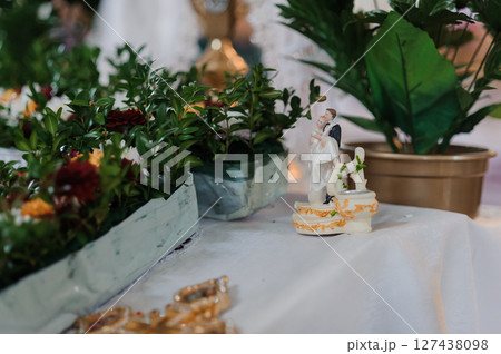Wedding cake topper figurine of a couple with a dog, set among lush greenery and floral arrangements on a white tablecloth Wedding cake topper figurine of a couple with a dog, set among lush greenery and floral arrangements on a white tablecloth 127438098