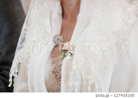 Close-up of a bride s lace jacket adorned with a brooch and a blush peach rose, showcasing intricate detailing and elegant wedding attire. 127438100