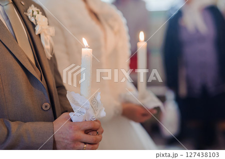 Close-up of wedding ceremony focusing on groom holding a lit candle with bride beside him during traditional rite 127438103
