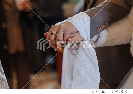 Romantic wedding moment with hands clasped, showcasing the wedding rings and elegant attire, focusing on connection and love. 127438105