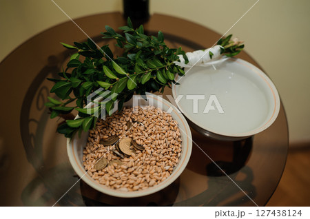 Greek wedding ritual preparation with olive branch crown, coins in pot, and traditional items for blessings and prosperity ceremony. Greek wedding ritual preparation with olive branch crown, coins in pot, and traditional items for blessings and prosperity ceremony. 127438124