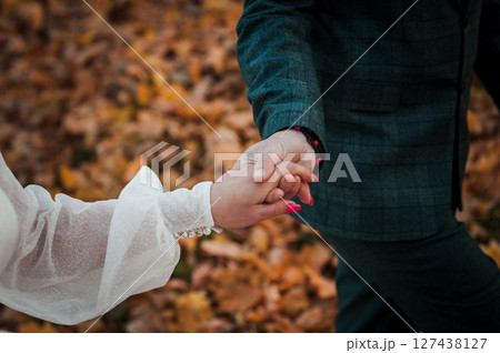 Couple holding hands while walking in autumn forest with falling golden leaves, intimate moment, plaid jacket, engagement, love, tenderness, relationship. 127438127