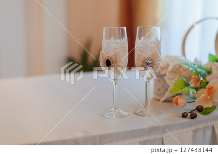 Wedding toasting flutes adorned with delicate lace and sparkling jewel accents, presented on a white tablecloth, symbolizing love and celebration. 127438144