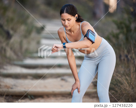 Fitness, running and woman with a smartwatch doing a cardio workout in the woods for health. Sports, wellness and athlete training for a race, marathon or exercise in nature in a forest with a watch. Fitness, running and woman with a smartwatch doing a cardio workout in the woods for health. Sports, wellness and athlete training for a race, marathon or exercise in nature in a forest with a watch. 127438220