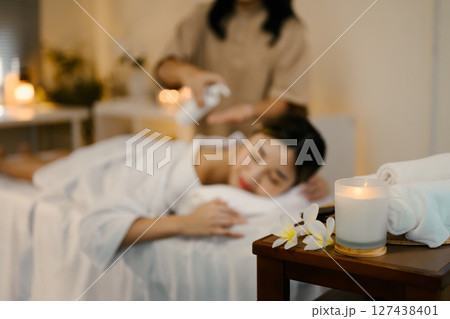 Aromatherapy candle and rolled towels in foreground, with female client on a massage table. 127438401