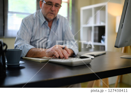Mature businessman calculating data or doing bookkeeping at a desk 127438411