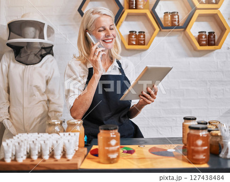 Small business woman, tablet and phone call in honey store for consulting, marketing or advertising in retail. Happy elderly female business owner working in a organic shop on phone with touchscreen 127438484