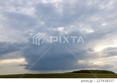 Dark storm clouds gather over a green hillside as the sun sets, signaling an approaching storm 127438527