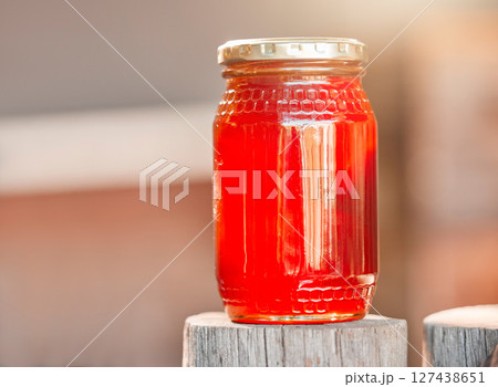 Honey, jar and background of glass, healthy nutrition and sugar production from bee farming, organic and sustainability from nature. Closeup bottle, liquid and honeycomb container, package and syrup 127438651