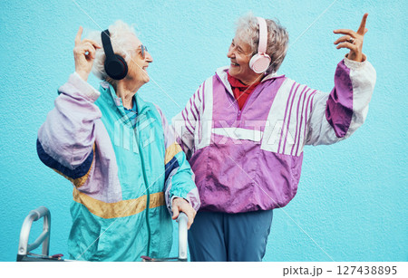 Friends, city and senior women with headphones on blue background wall listening to audio, music and radio. Fashion, style and elderly females enjoy retirement, freedom and dancing in urban town Friends, city and senior women with headphones on blue background wall listening to audio, music and radio. Fashion, style and elderly females enjoy retirement, freedom and dancing in urban town 127438895