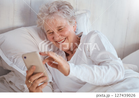 Happy elderly woman, bed or phone on social media for meme, comic or joke on internet. Senior lady, bedroom or smartphone tech with laugh at social network, funny video or email on web, app or online Happy elderly woman, bed or phone on social media for meme, comic or joke on internet. Senior lady, bedroom or smartphone tech with laugh at social network, funny video or email on web, app or online 127439026