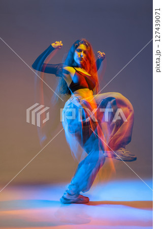 Stylish jazz-funk dancer in motion under vivid studio lighting, with glowing colors and urban dance energy. 127439071