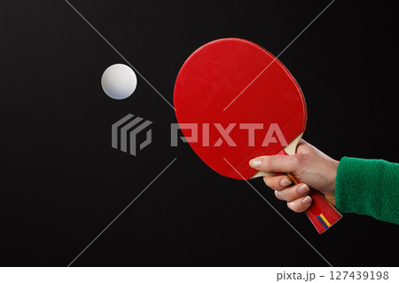 Close-up of red table tennis paddle and white ball in motion against black background, minimal sports concept. 127439198