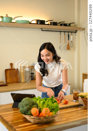 Happy woman slicing tomatoes and cooking healthy meal with online recipe 127440299