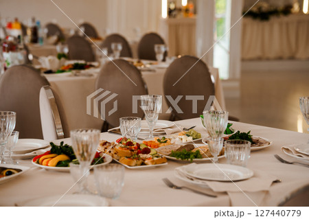 Elegant Wedding Reception Table Setting with Gourmet Appetizers, Glassware, White Linens, and Soft Lighting in a Bright Banquet Hall 127440779