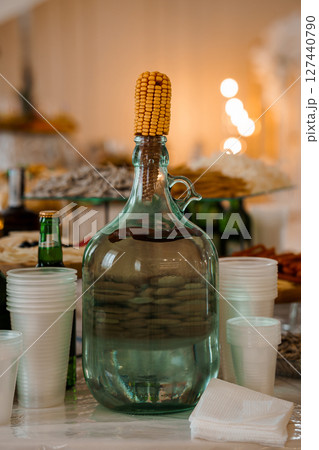 Rustic Autumn Still Life with Vintage Jug, Corn Decoration, Stacked Cups, and Festive Table Setting in Warm, Bokeh-Lit Interior. 127440790
