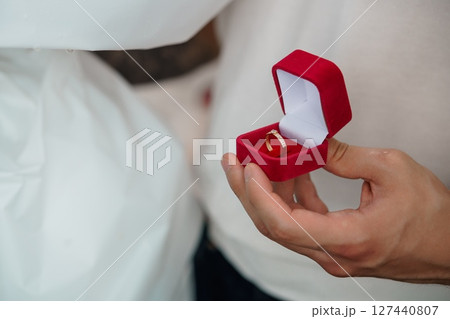 Wedding Rings Exchange Ceremony, Close-Up of Hands Holding Red Box, Symbolic Love Commitment, Golden Bands, Elegant Style. Wedding Rings Exchange Ceremony, Close-Up of Hands Holding Red Box, Symbolic Love Commitment, Golden Bands, Elegant Style. 127440807