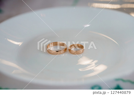 Two Golden Wedding Rings on a White Plate, Close-up Shot with Blurred Background, Love, Marriage, Commitment, Romance, Gold Color Tone. Two Golden Wedding Rings on a White Plate, Close-up Shot with Blurred Background, Love, Marriage, Commitment, Romance, Gold Color Tone. 127440879
