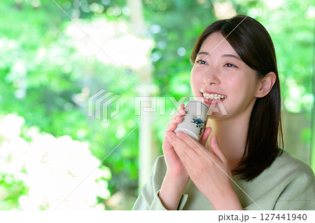 自然光が差し込む室内で湯呑みを持つ女性がさわやかな笑顔を見せる夏のお茶時間ポートレート 127441940