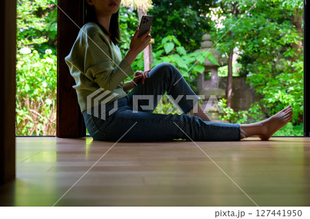 自然光の差し込む縁側で足を伸ばしながらスマホを操作する女性の穏やかな夏の夕暮れ時間 自然光の差し込む縁側で足を伸ばしながらスマホを操作する女性の穏やかな夏の夕暮れ時間 127441950