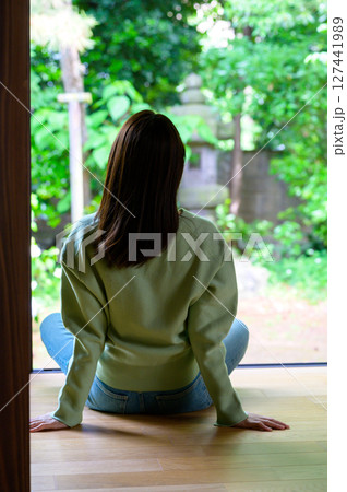 縁側に両手をつきながら深呼吸するように腰かけた女性の落ち着いた後ろ姿の夏の朝風景 縁側に両手をつきながら深呼吸するように腰かけた女性の落ち着いた後ろ姿の夏の朝風景 127441989
