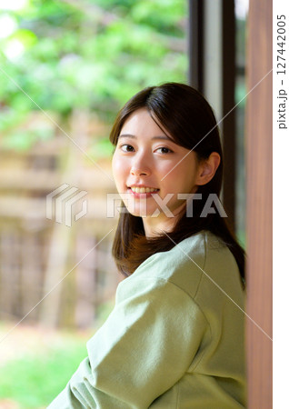 緑を背景に柔らかい表情で微笑む女性の穏やかな夏の縁側ポートレート 127442005