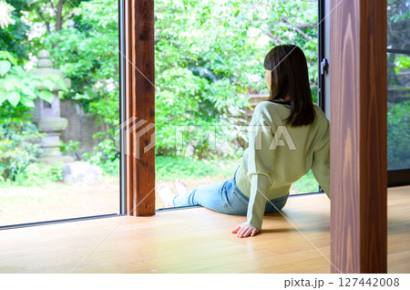 縁側で手をついて座る女性が外の自然を見ながらのびやかに過ごす夏の休日の一場面 127442008
