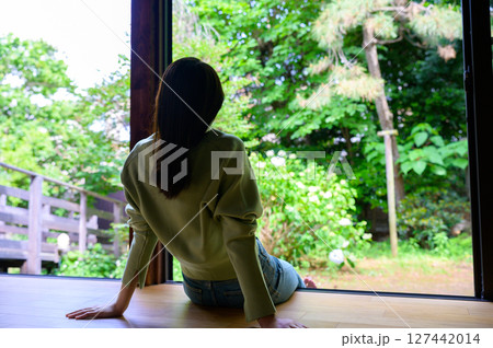 女性が縁側に座りながら外の自然に目を向けている穏やかで落ち着いた夏の時間 127442014
