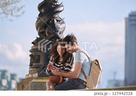 Couple, phone and travel holiday while at statue doing search on internet for map information on tourist trip. Man and woman with cellphone for social media content on foreign city journey in London 127442528