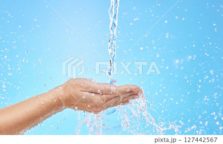 Hand, water and cleaning with a splash in studio on a blue background for hygiene or hydration. Mockup, health and wellness with a female washing under a water splash in the bathroom for skincare 127442567