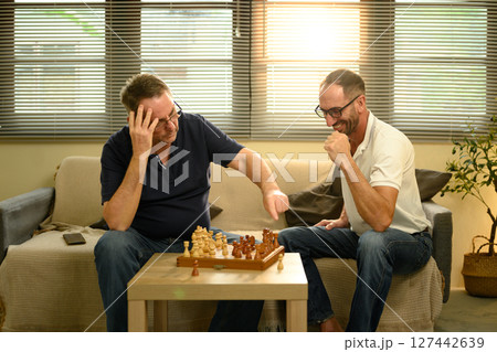 Mature father and son sit on a couch, focused on a strategic game of chess. Father day concept Mature father and son sit on a couch, focused on a strategic game of chess. Father day concept 127442639