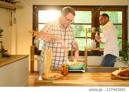 Happy senior man and his son enjoy preparing a home cooked meal in a kitchen. Father day concept 127442691