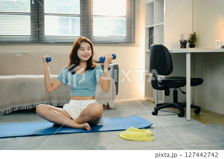 Young woman lifting dumbbells during home workout Young woman lifting dumbbells during home workout 127442742