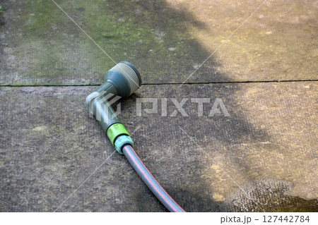 Garden Hose and Nozzle on a Concrete Patio 127442784