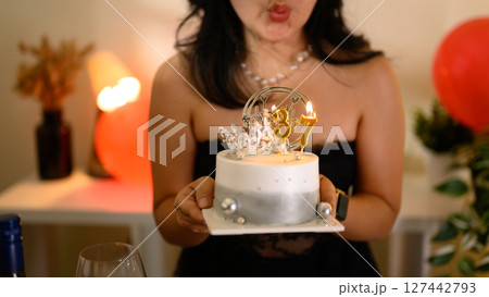 Glamorous birthday celebration with a fashionable woman blowing out candles on a 37th birthday cake Glamorous birthday celebration with a fashionable woman blowing out candles on a 37th birthday cake 127442793