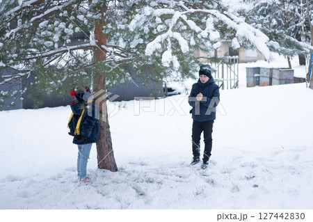 Winter fun: Two children play in the snow near a snow-covered tree. One hides behind the tree, the other stands warming their hands. Winter fun: Two children play in the snow near a snow-covered tree. One hides behind the tree, the other stands warming their hands. 127442830