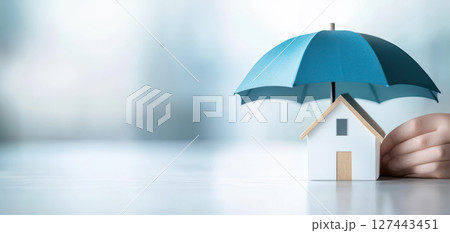 small house model is protected by blue umbrella, symbolizing safety and security 127443451