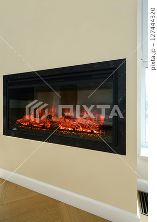 Modern electric fireplace with glowing logs enhancing cozy living room ambiance Modern electric fireplace with glowing logs enhancing cozy living room ambiance 127444320