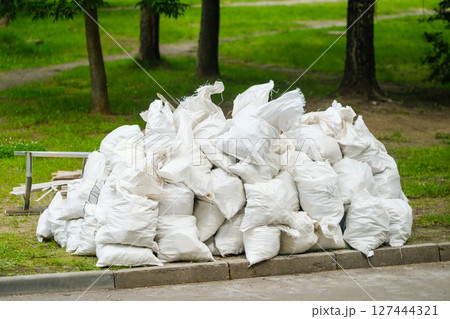 Waste material stacked in white bags in a park area during daytime Waste material stacked in white bags in a park area during daytime 127444321