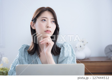 部屋でパソコンをみて考える悩む迷うかわいい女性　ちょっと真剣なネガティブイメージ　転職どうしようかな 127444512